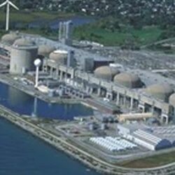 An aerial view of a power plant with water in the foreground.