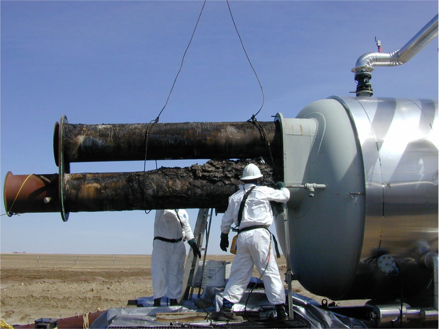 Two men in white suits working on a pipeline.